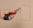person cutting rectangular hole in drywall with drywall saw